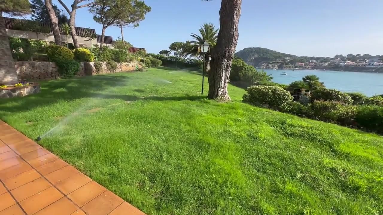 Aspersor funcionando sobre césped en un jardín residencial junto al mar